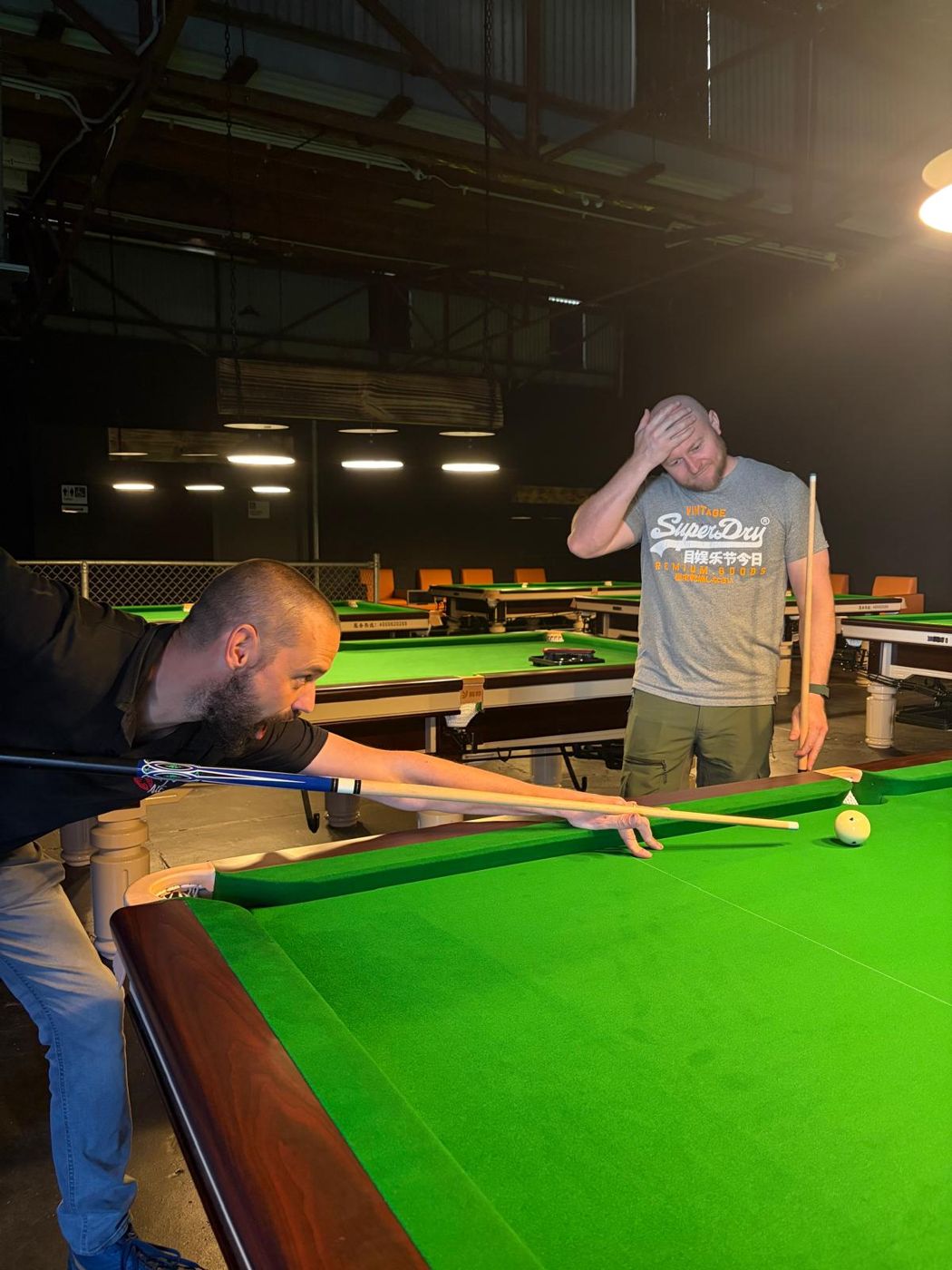 One mate lines up a shot while another holds his cue and his head in mock despair